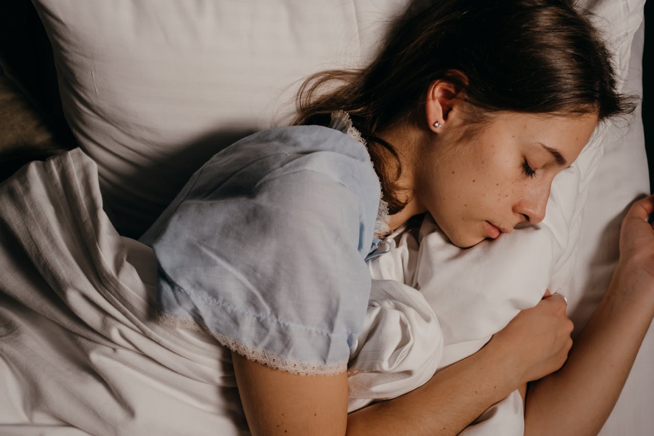 services-01 A serene young woman peacefully sleeping on a white pillow indoors at night.