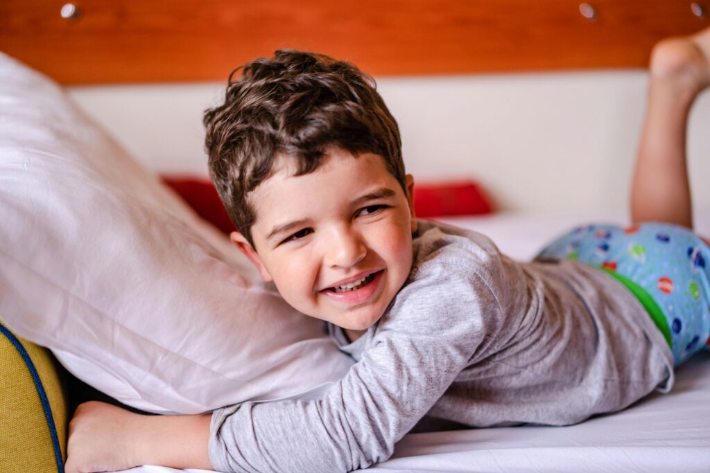 Smiling child in pajamas lying on a bed indoors. Warm and cozy home setting.